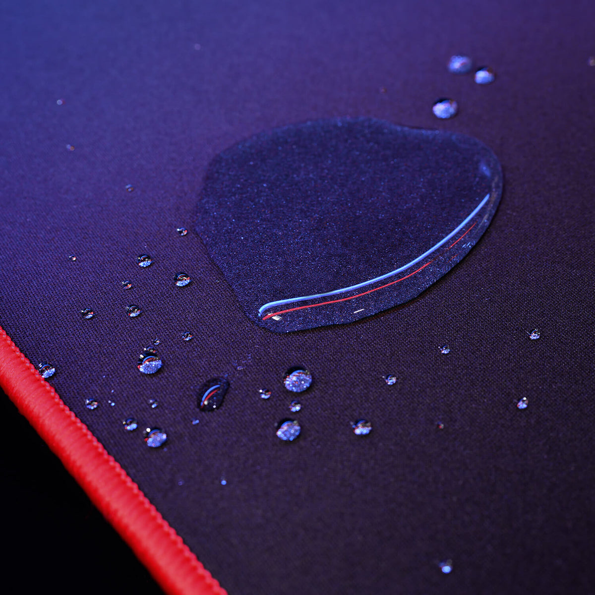 Water droplets on a dark surface with a red edge, lit by blue and purple light.