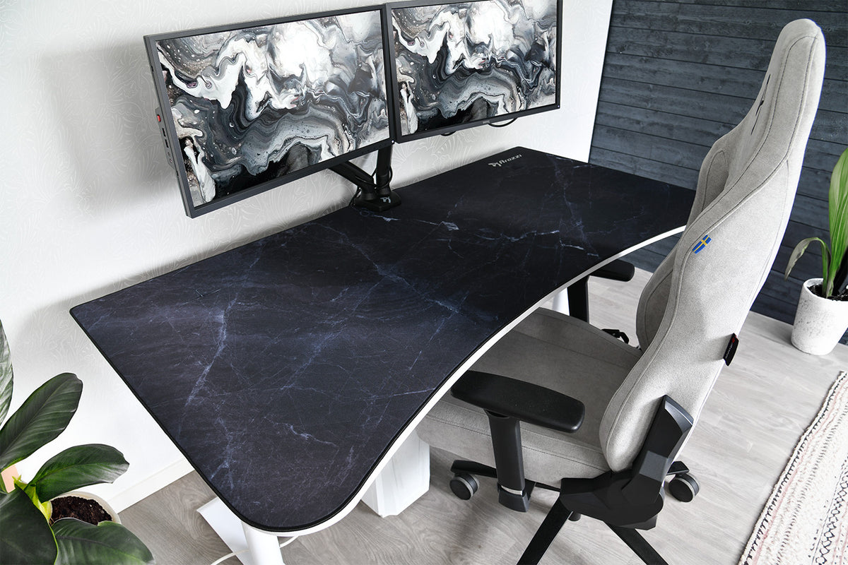 Dual monitors on a black marble desk with a gray chair and potted plants nearby.
