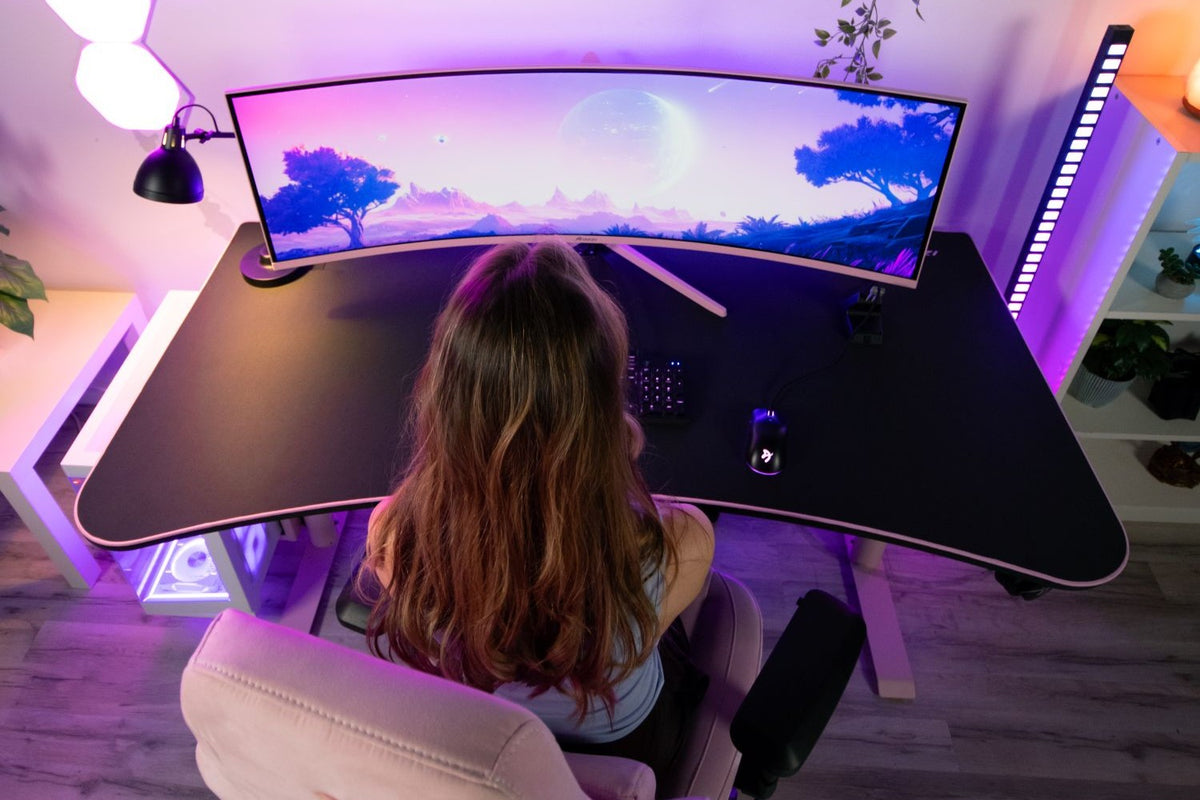 Woman at a curved ultrawide monitor with a cosmic landscape, seen from above.