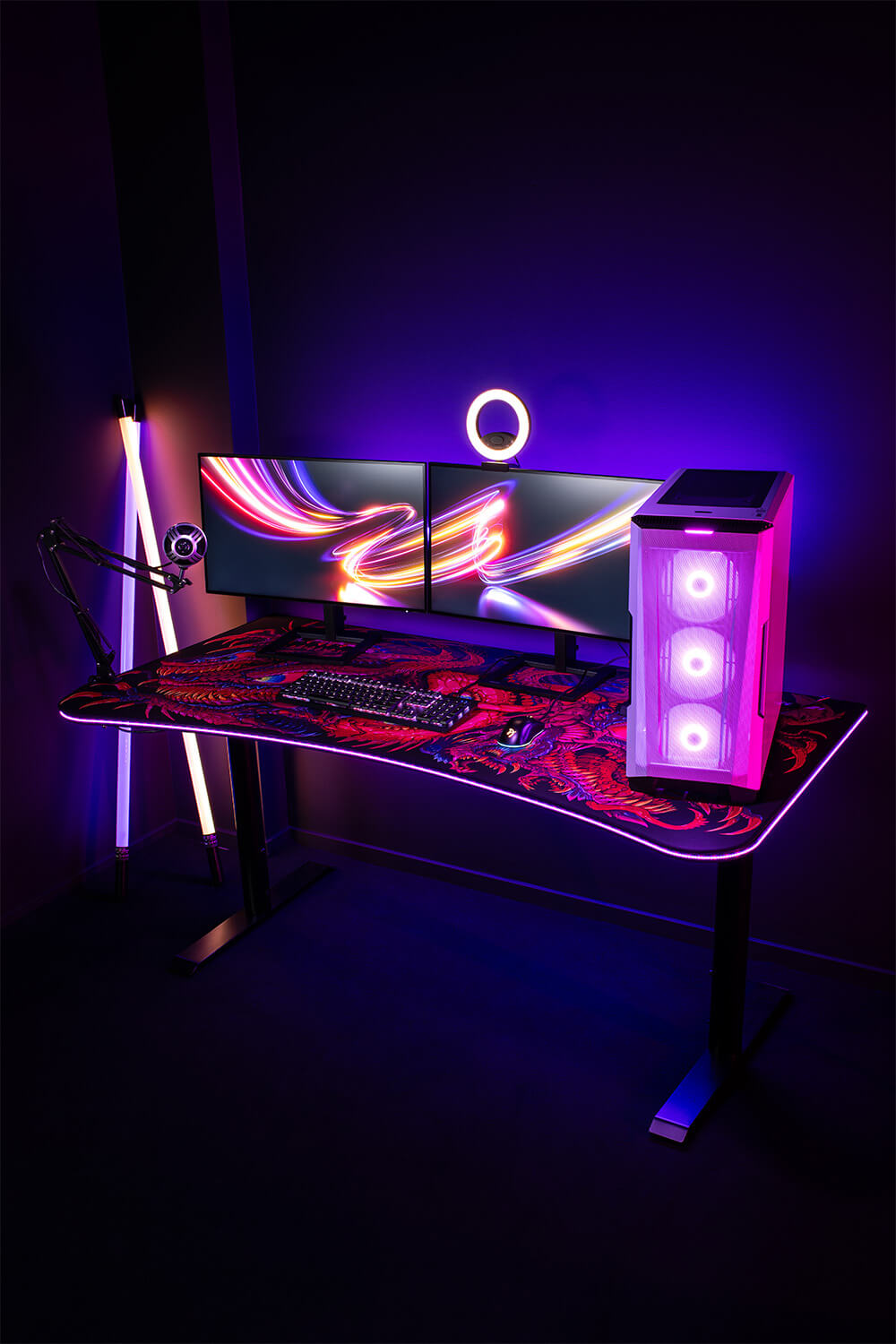 A gaming desk setup with dual monitors, RGB lights, and a glowing PC case in a dark room.