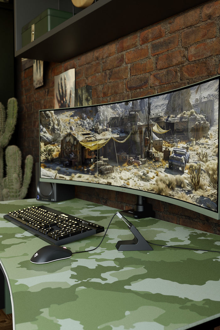 Curved monitor on a camo desk displays a detailed post-apocalyptic game scene.