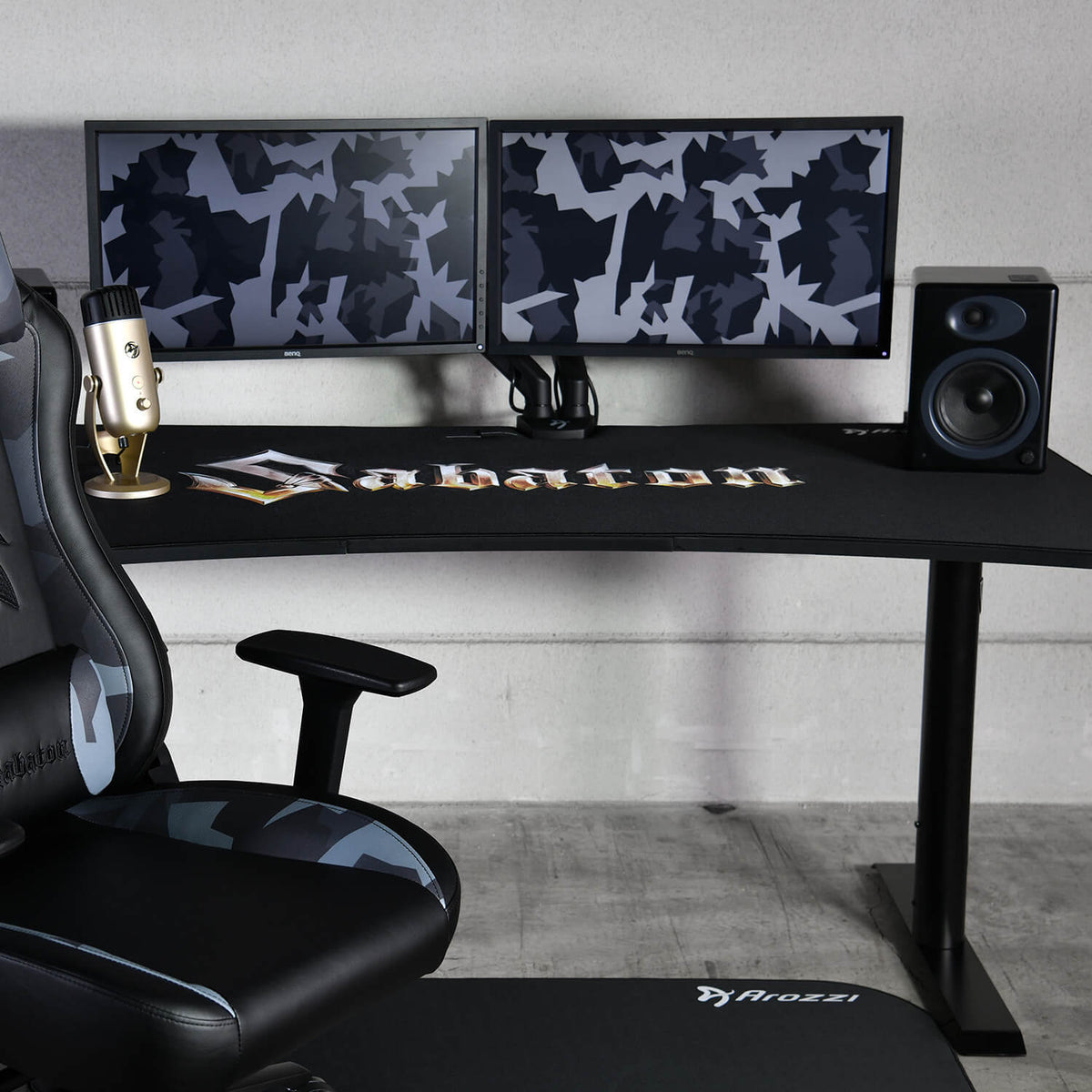 Dual monitors, mic, and chair sit atop the Arozzi Arena Gaming Desk Sabaton Edition.