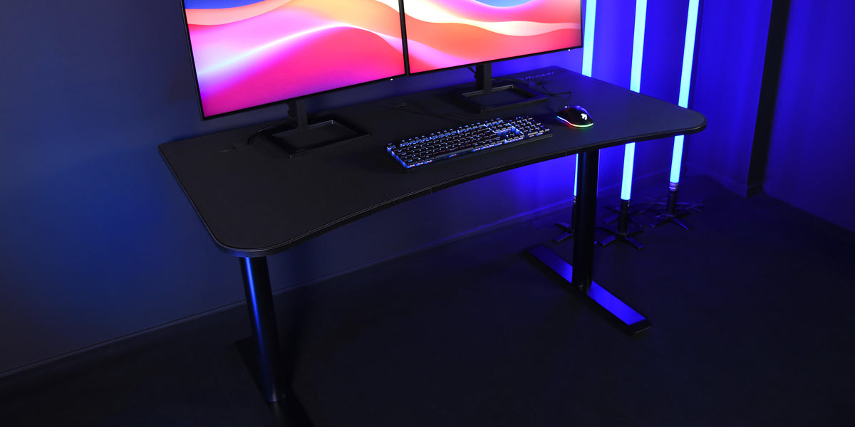 Black desk with dual monitors, keyboard, and mouse, illuminated by blue LED lights.