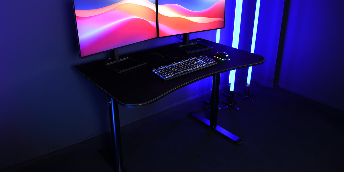 Dual monitor setup on a black desk with keyboard and mouse, blue ambient lighting.