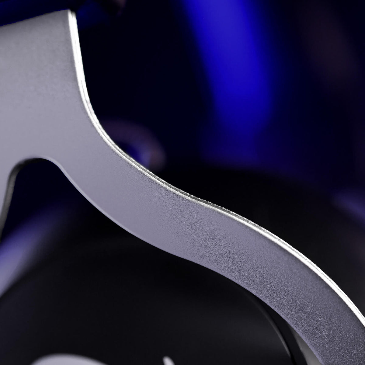 Curved silver metal piece with blurred blue and black background, possibly a headphone part.