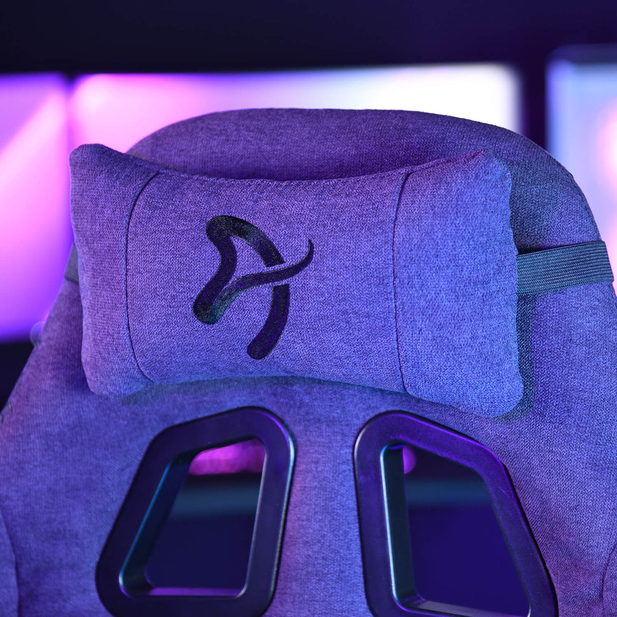 Close-up of a gaming chair headrest with a pillow and logo, in purple lighting.