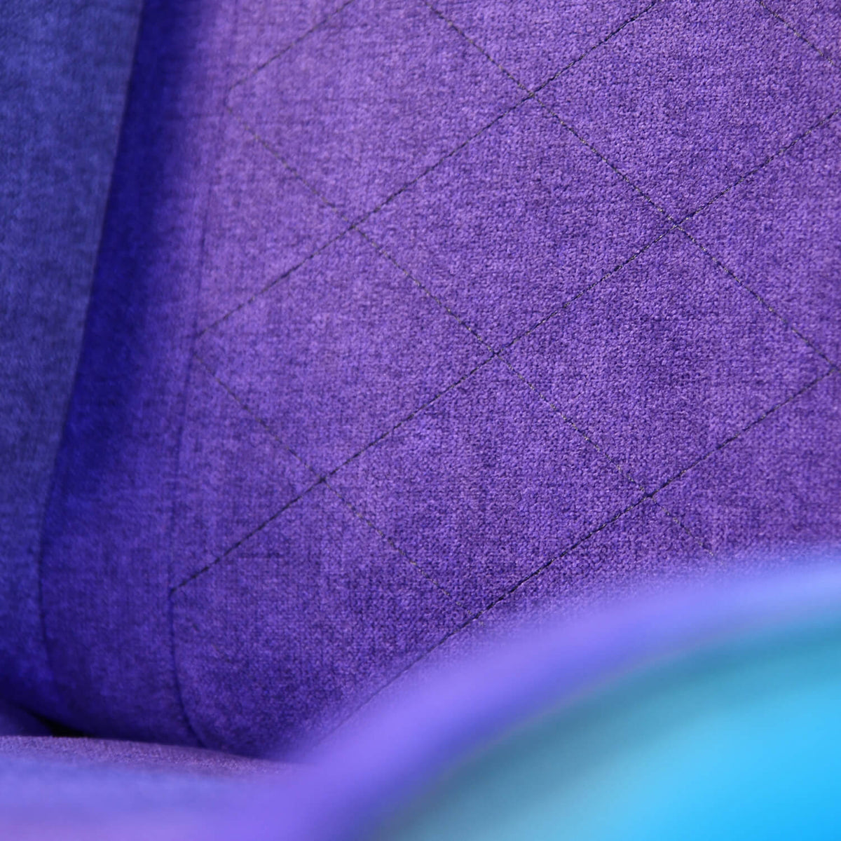 Close-up of purple fabric with diamond stitching and a blurred blue edge in the foreground.