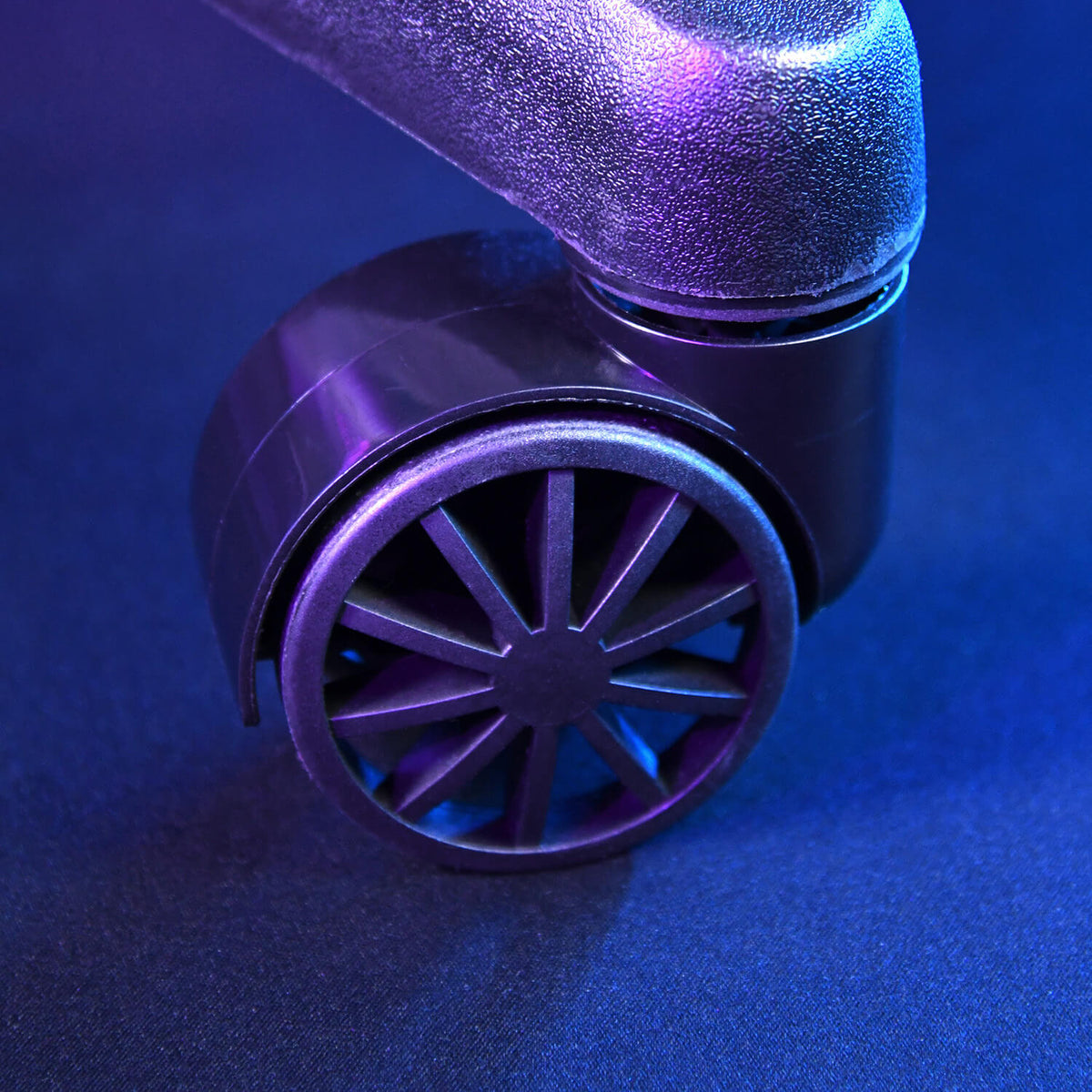 Close-up of a black office chair wheel on a dark surface with blue and purple lighting.