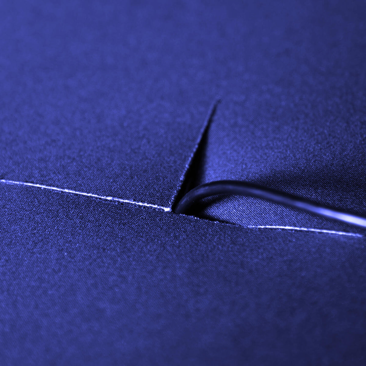 Closeup of a sewing needle and thread passing through dark blue fabric.