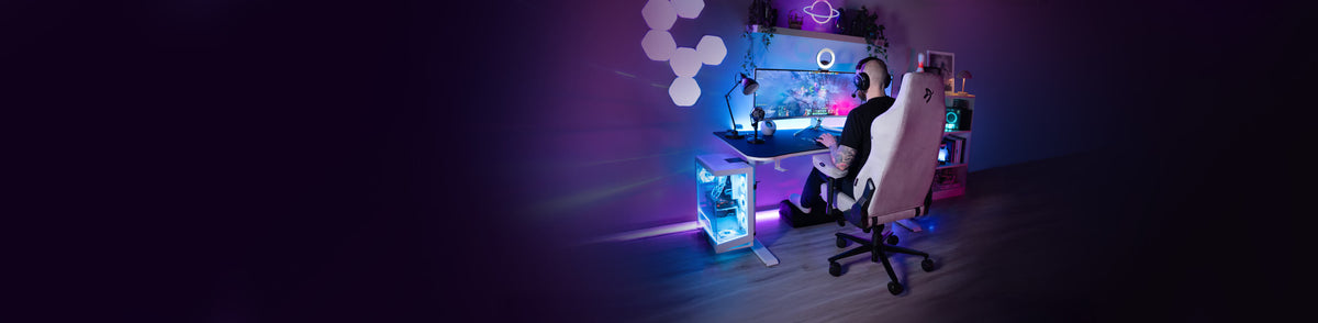 Person gaming at a colorful desk setup with LED lights, screens, and gaming chair.