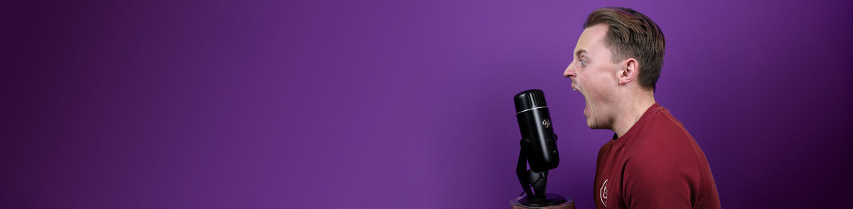 Man in red shirt shouting into a black microphone against a purple background.