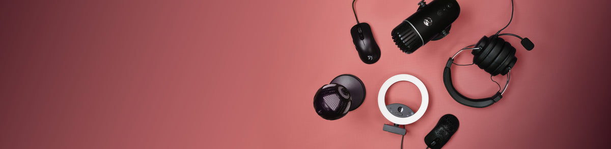 Headphones, microphones, mice, and a ring light arranged on a pink background.