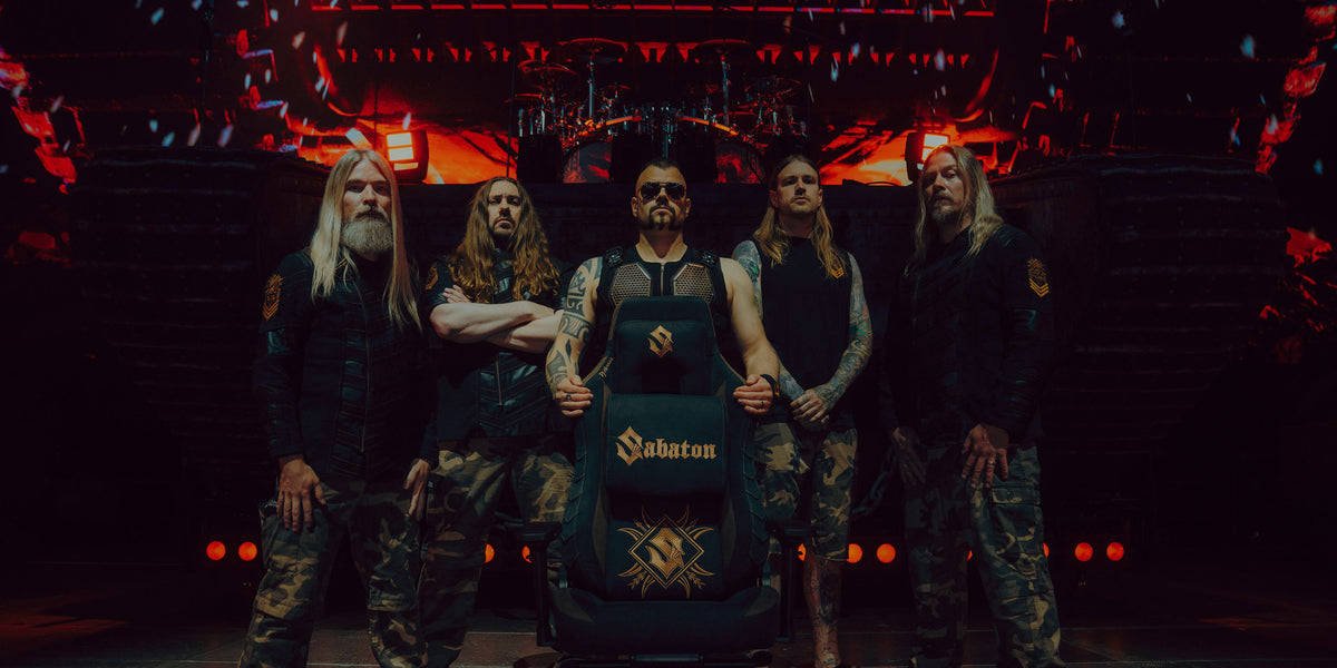Five men in camo pants pose onstage with a chair labeled Sabaton and dramatic red lighting.