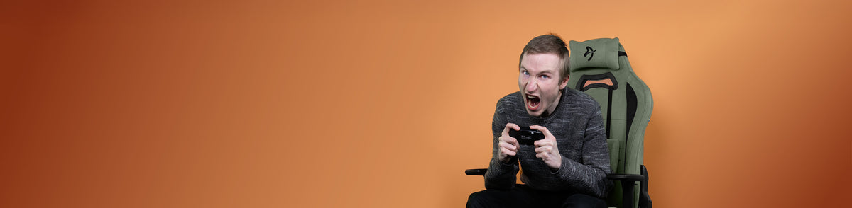 Man in a gaming chair excitedly playing video games against an orange background.