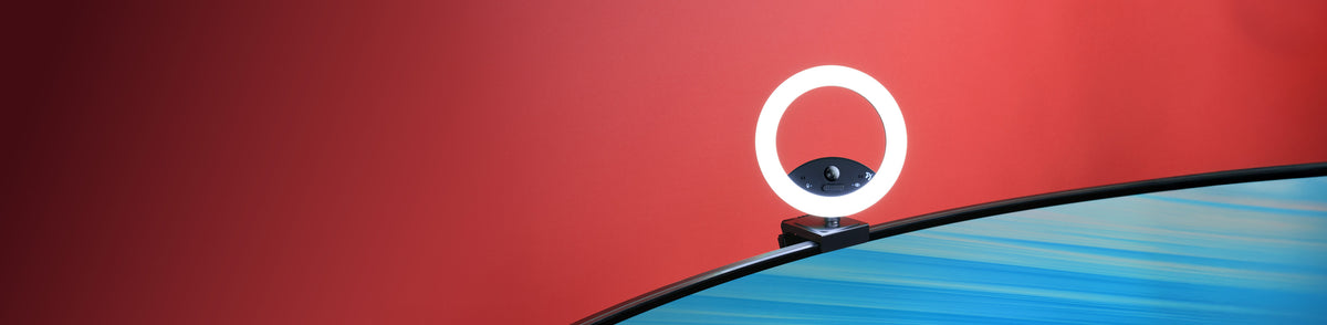 A ring light attached to the top edge of a curved monitor against a red background.