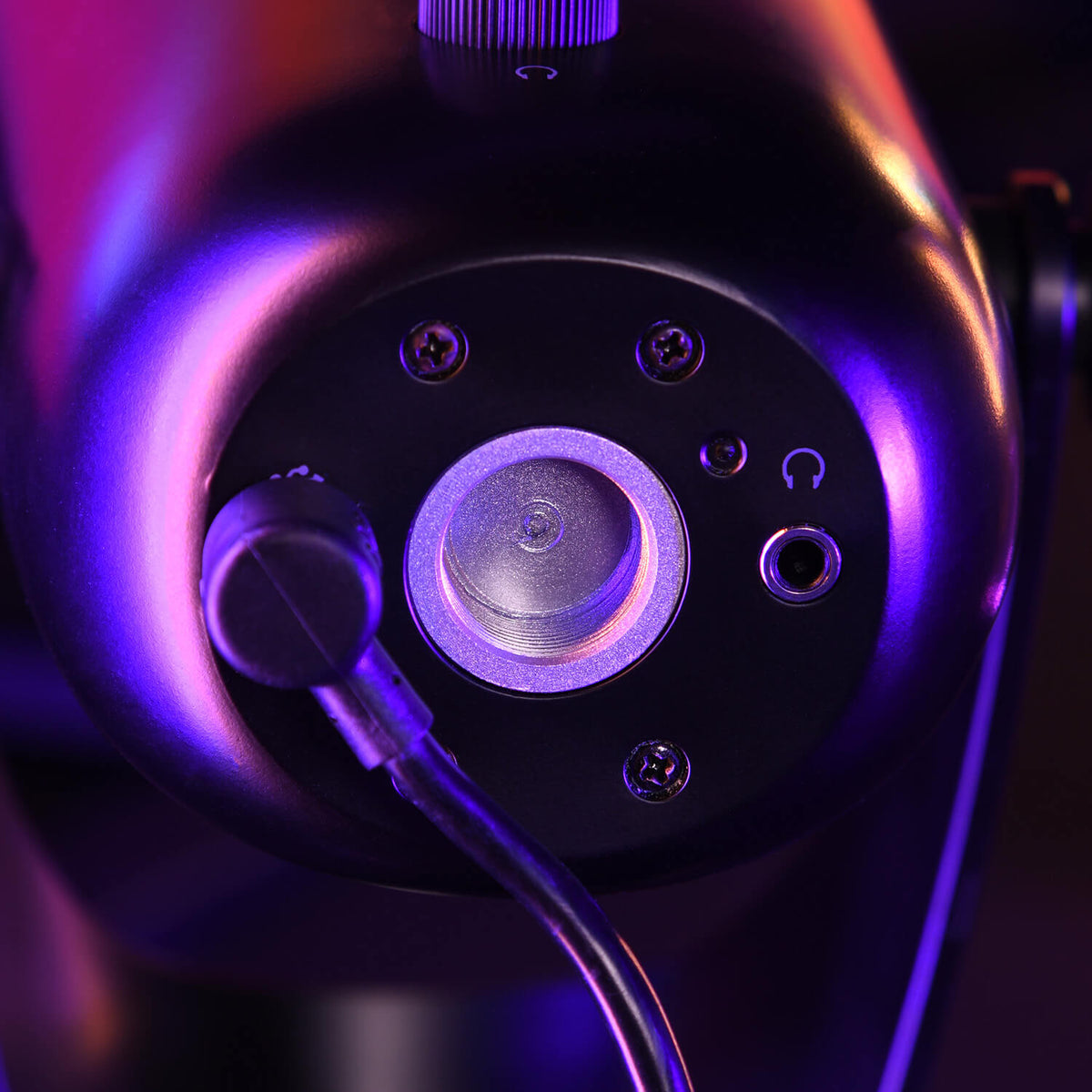 Close-up of a microphone base with cable plugged in, lit by purple and orange lights.