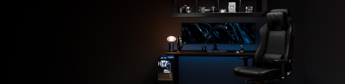 Modern black gaming desk setup with monitor, lamp, camera shelf, and black gaming chair.