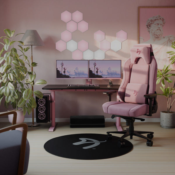 Pink gaming setup with dual monitors, pink chair, plants, and hexagonal wall lights.