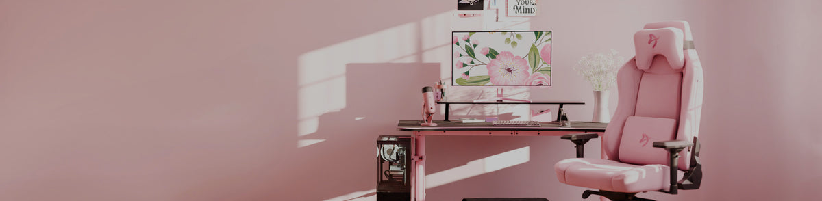 Pink gaming chair and desk setup with floral monitor and soft pink decor in sunlight.