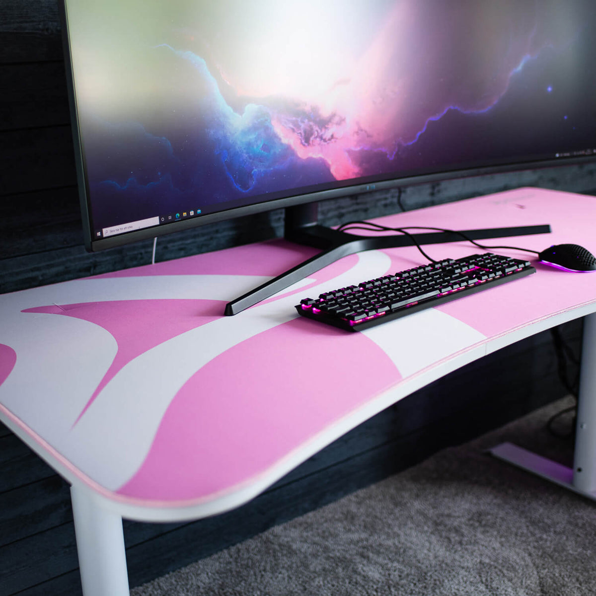 Curved monitor, keyboard, and mouse on a pink and white desk with an Arozzi Arena Mousepad.