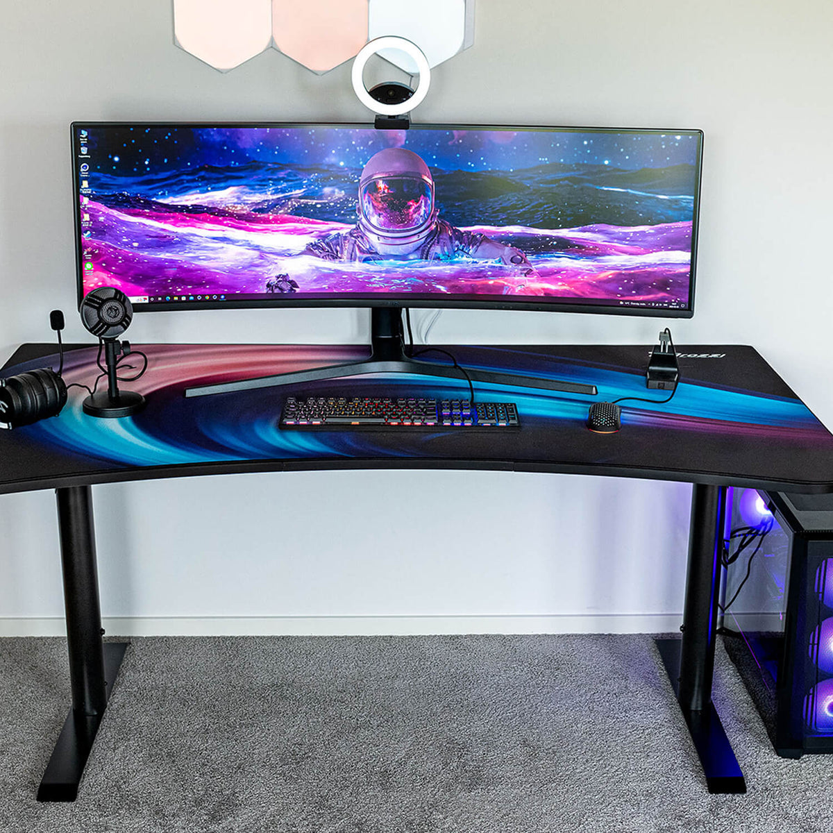 Curved desk with wide monitor, astronaut wallpaper, and Arozzi Arena water-resistant mousepad.
