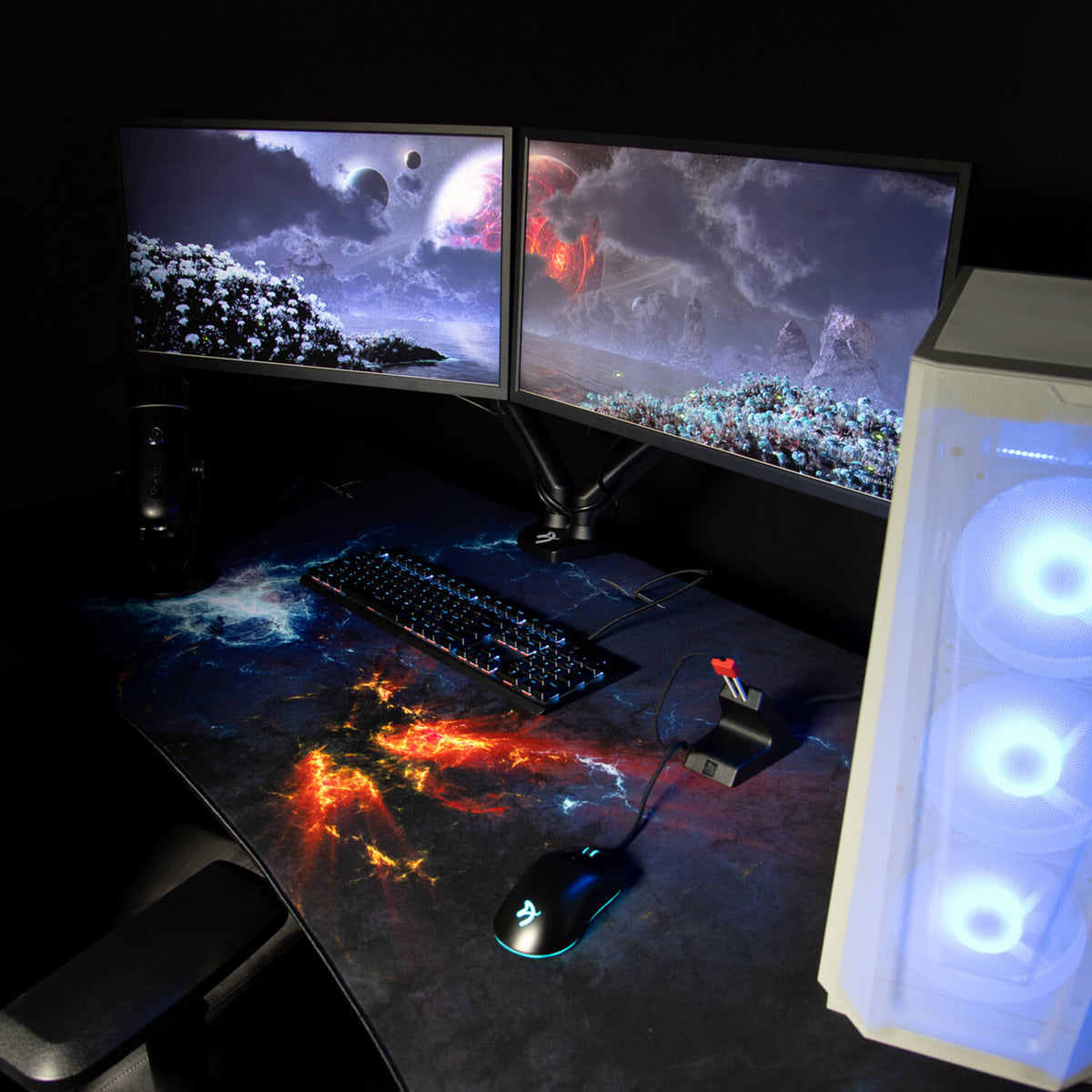 Dual monitors, space wallpaper, gaming keyboard, Arozzi Arena Mousepad, and glowing PC on desk.