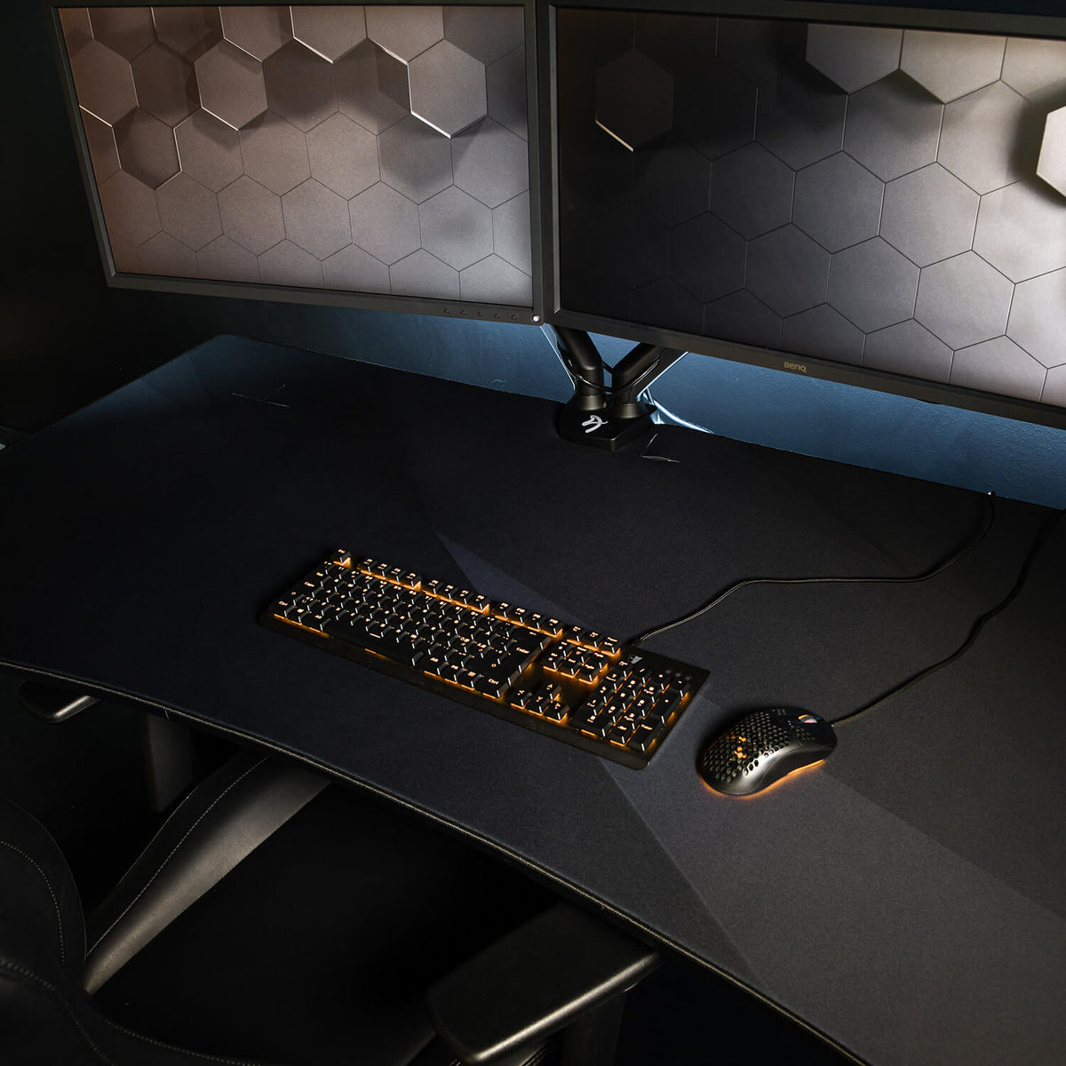 Dual monitors, keyboard, and mouse on a large desk with the Arozzi Arena Mousepad in dim light.