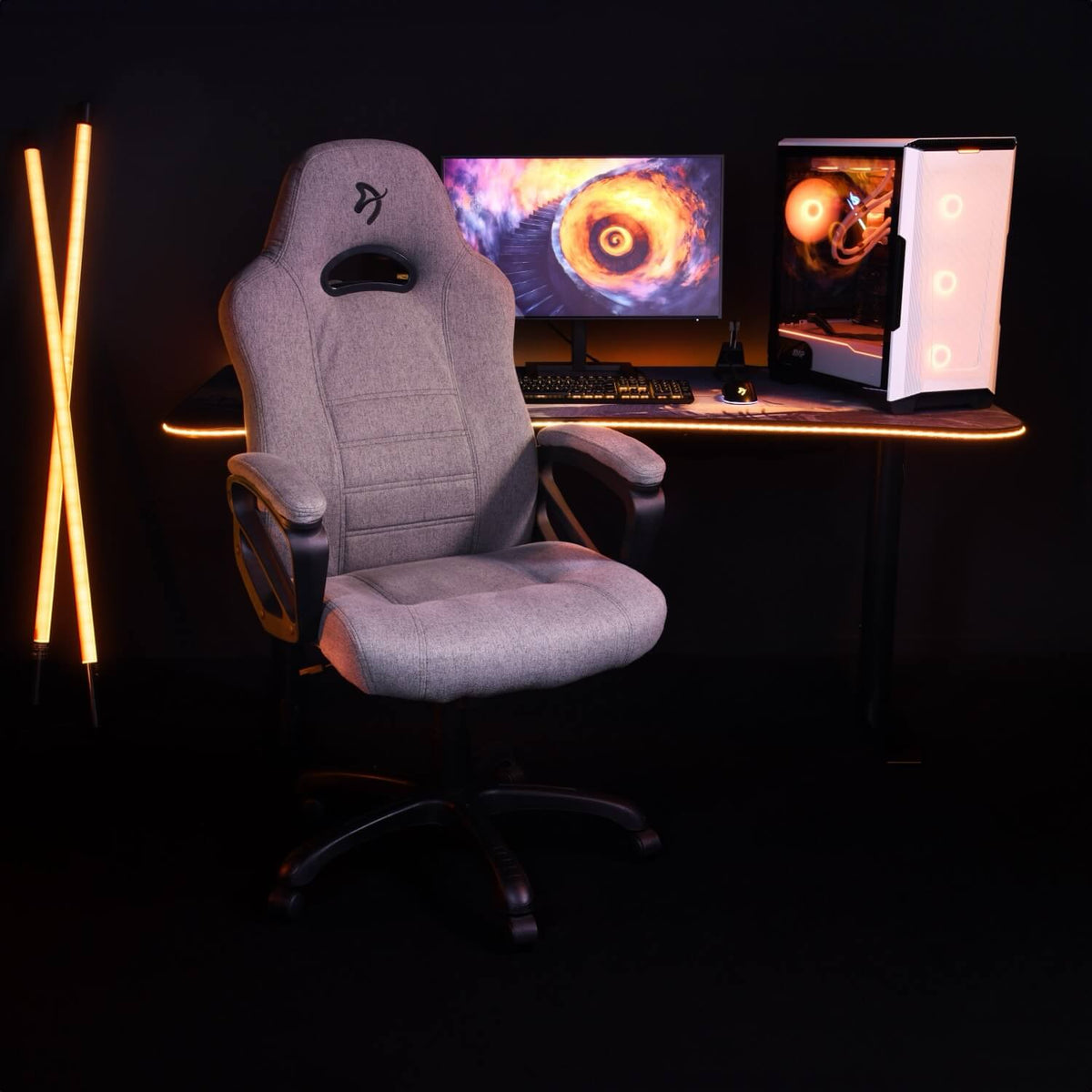 Gray office chair in front of a lit-up PC gaming setup with dual orange LED light sticks.