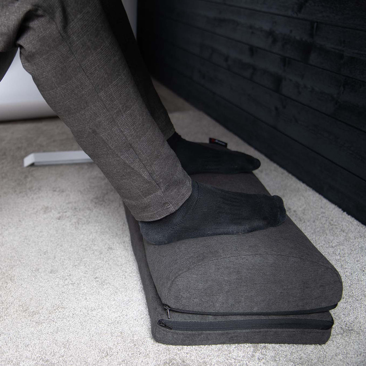 Person with black socks resting feet on Arozzi Europe Footrest on a carpeted floor.