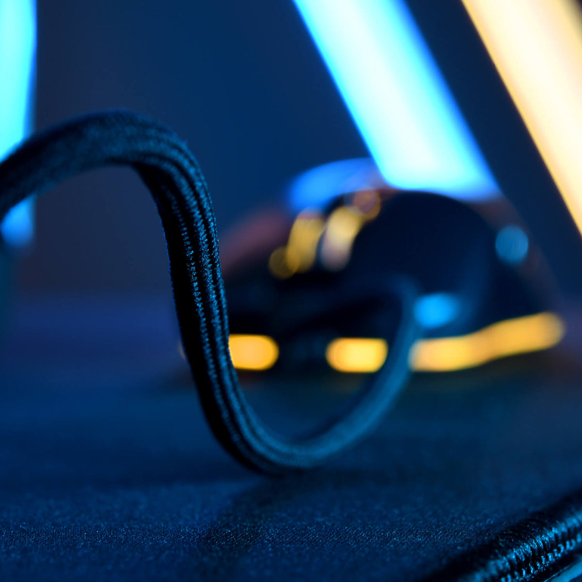 Close-up of a braided computer mouse cable on a dark surface with blue and yellow lights.