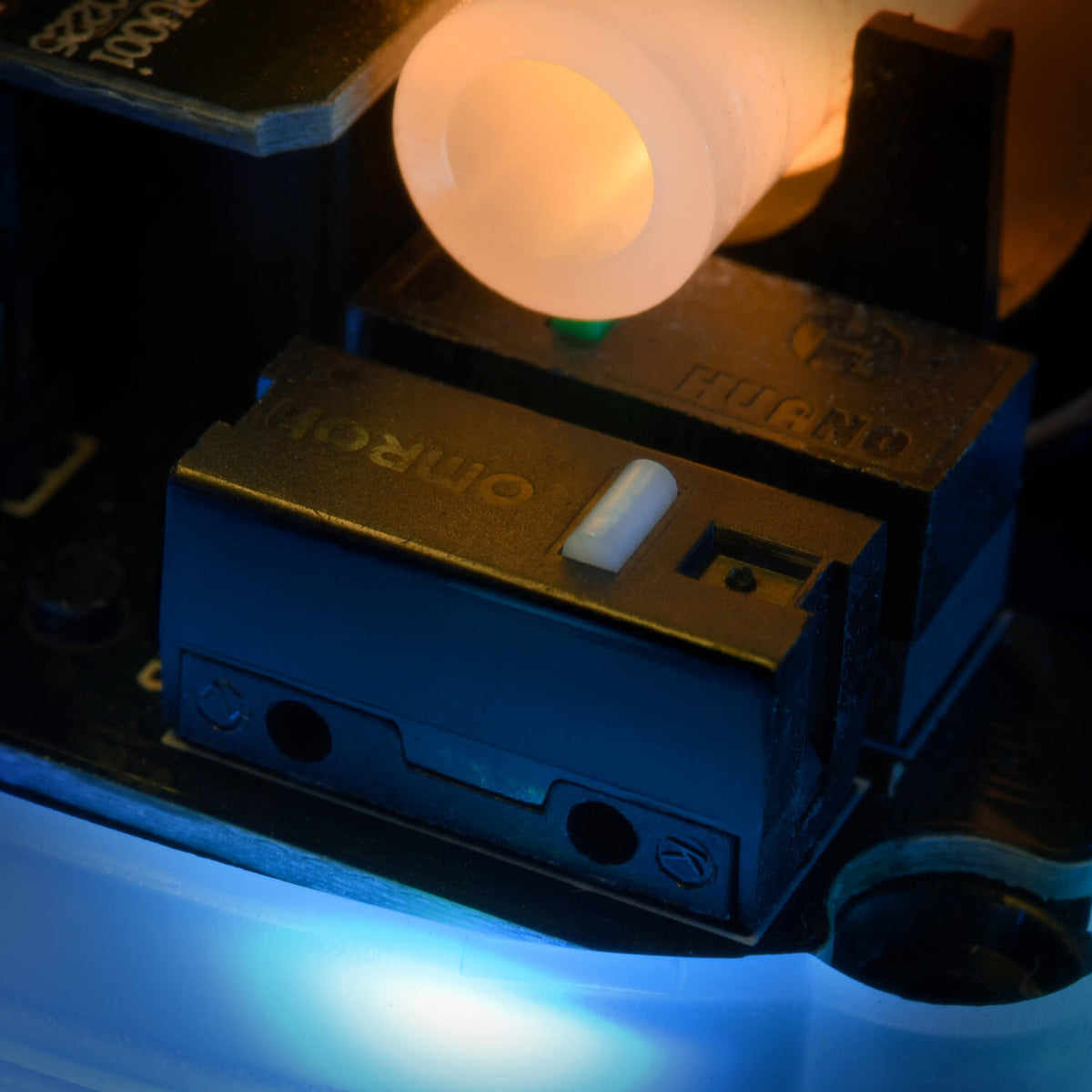 Close-up of a black Omron micro switch with an orange plastic part above it and blue light below.