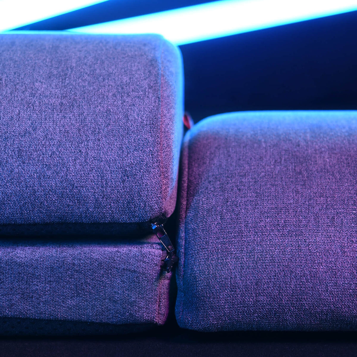 Close-up of two purple fabric cushions with a zipper, lit by blue and pink neon lights.