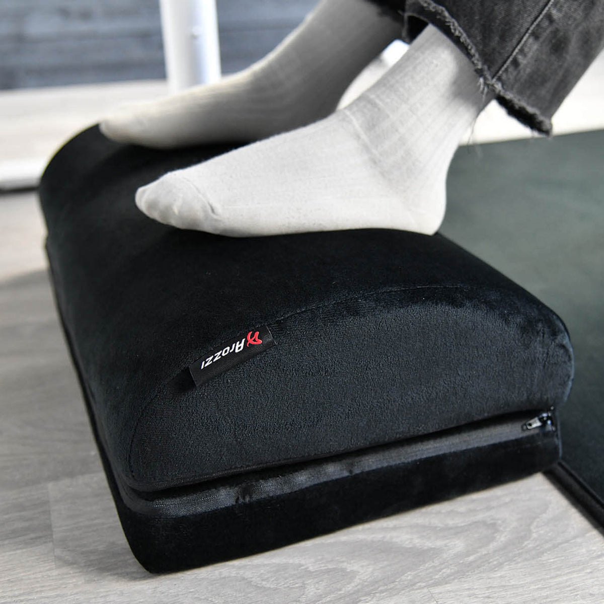 White socks on Arozzi Europe Footrest, memory foam cushion, light wood floor.