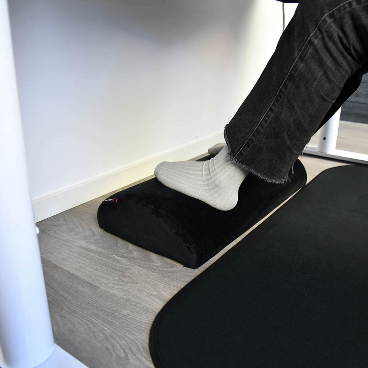 Someone rests their feet on an Arozzi Europe Footrest under a desk.