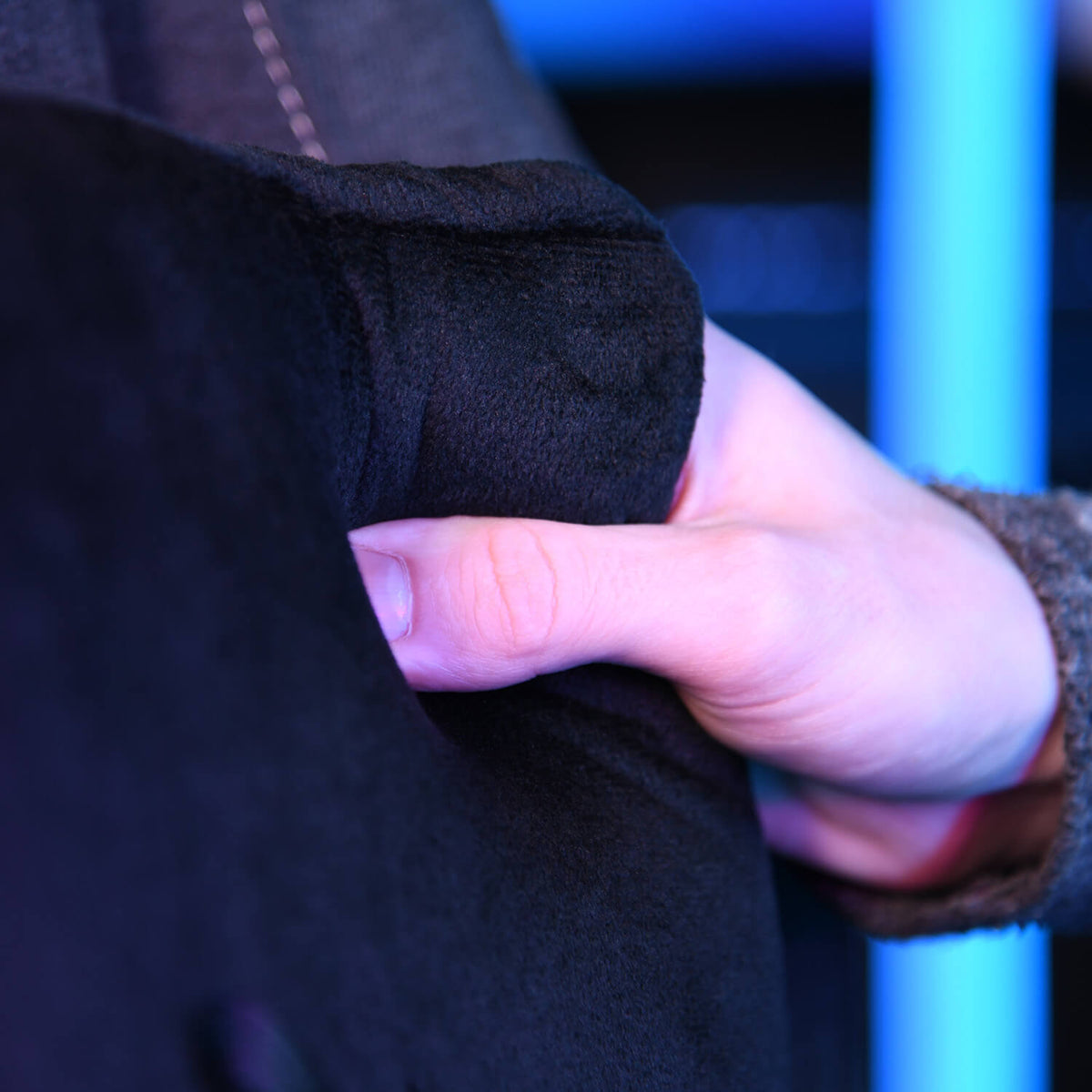 A hand holds and squeezes a soft, black fabric under blue lighting.