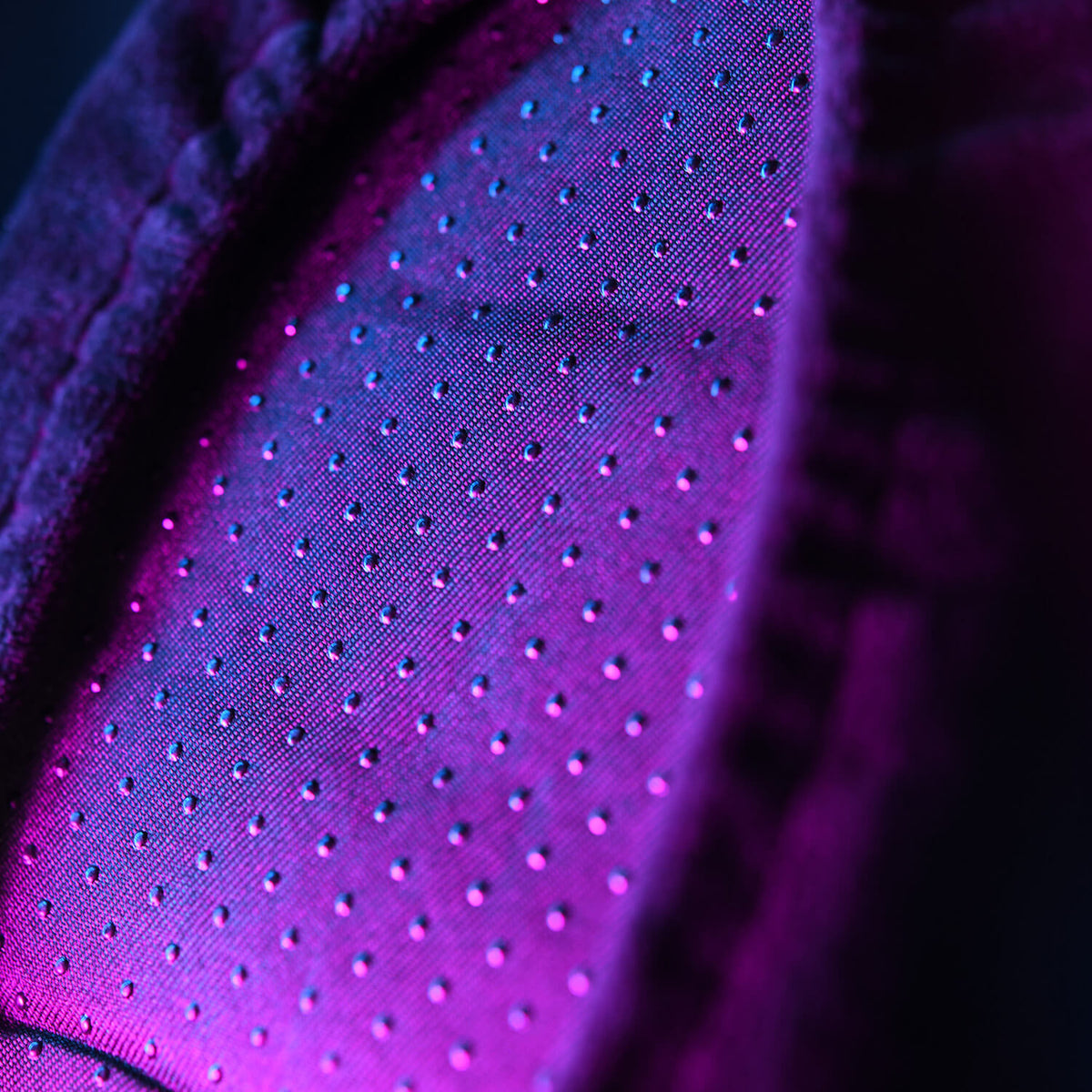 Close-up of perforated fabric with purple and blue lighting.