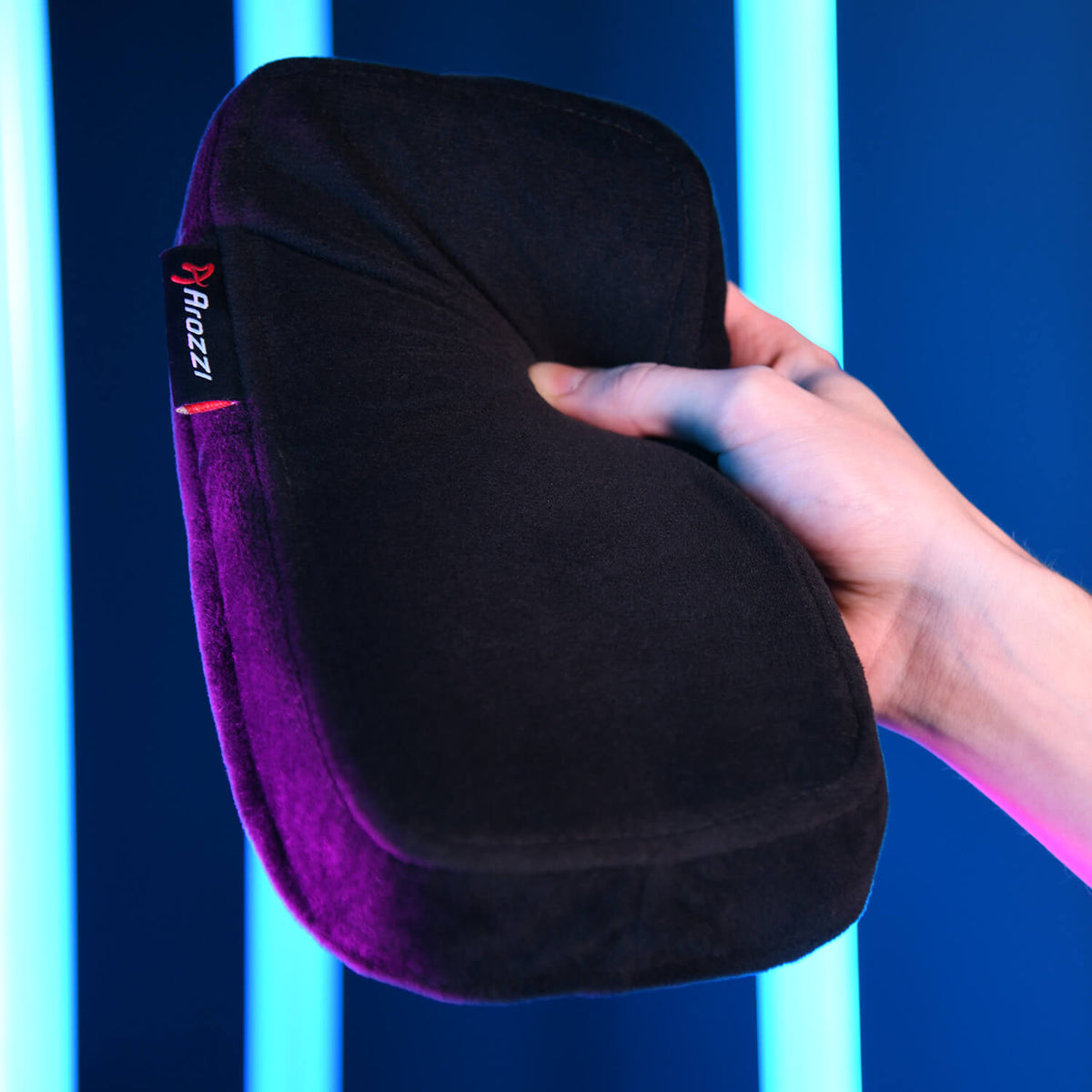 Hand holding a black cushion with an Arozzi tag, blue neon lights in the background.