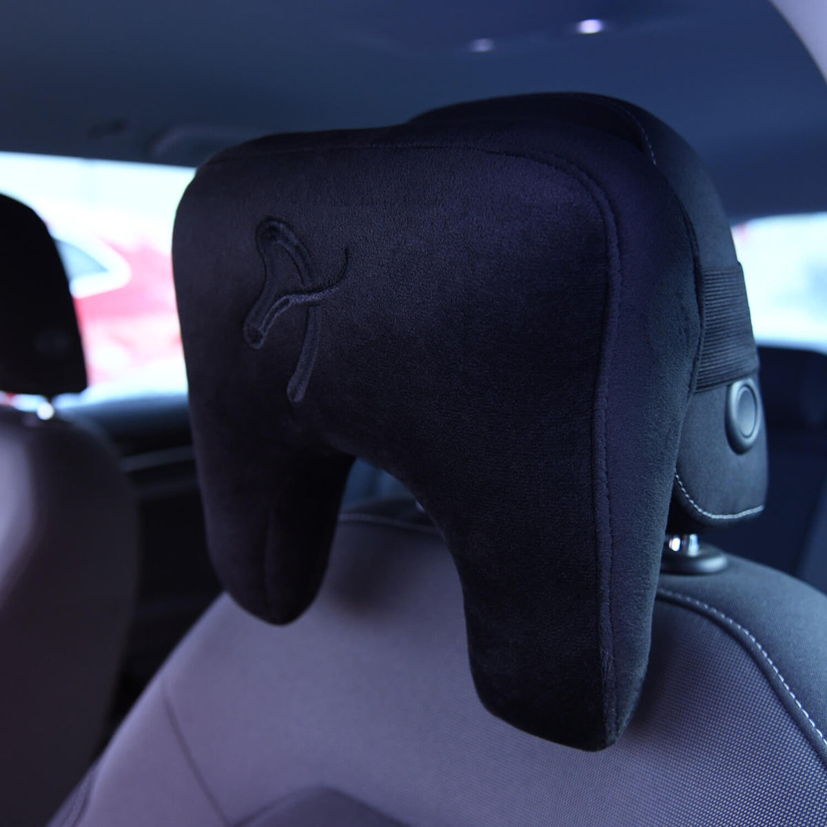 Black cushioned neck pillow attached to a car seat headrest inside a vehicle.