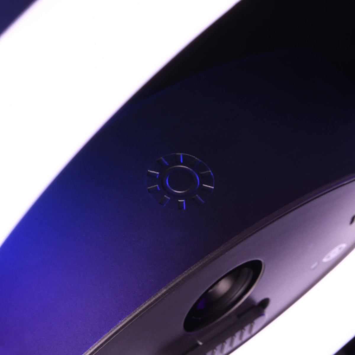 Close-up of a black device with a textured circular logo and a lens, illuminated by purple light.