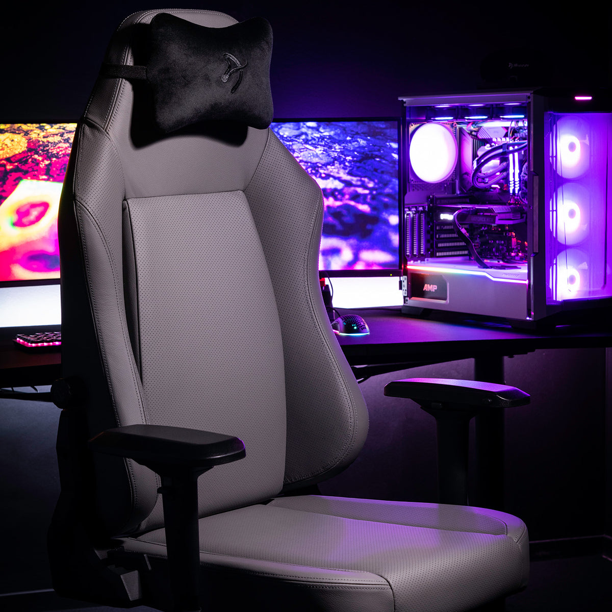 Primo - Full Premium Leather by Arozzi Europe in front of a glowing PC and colorful monitors.