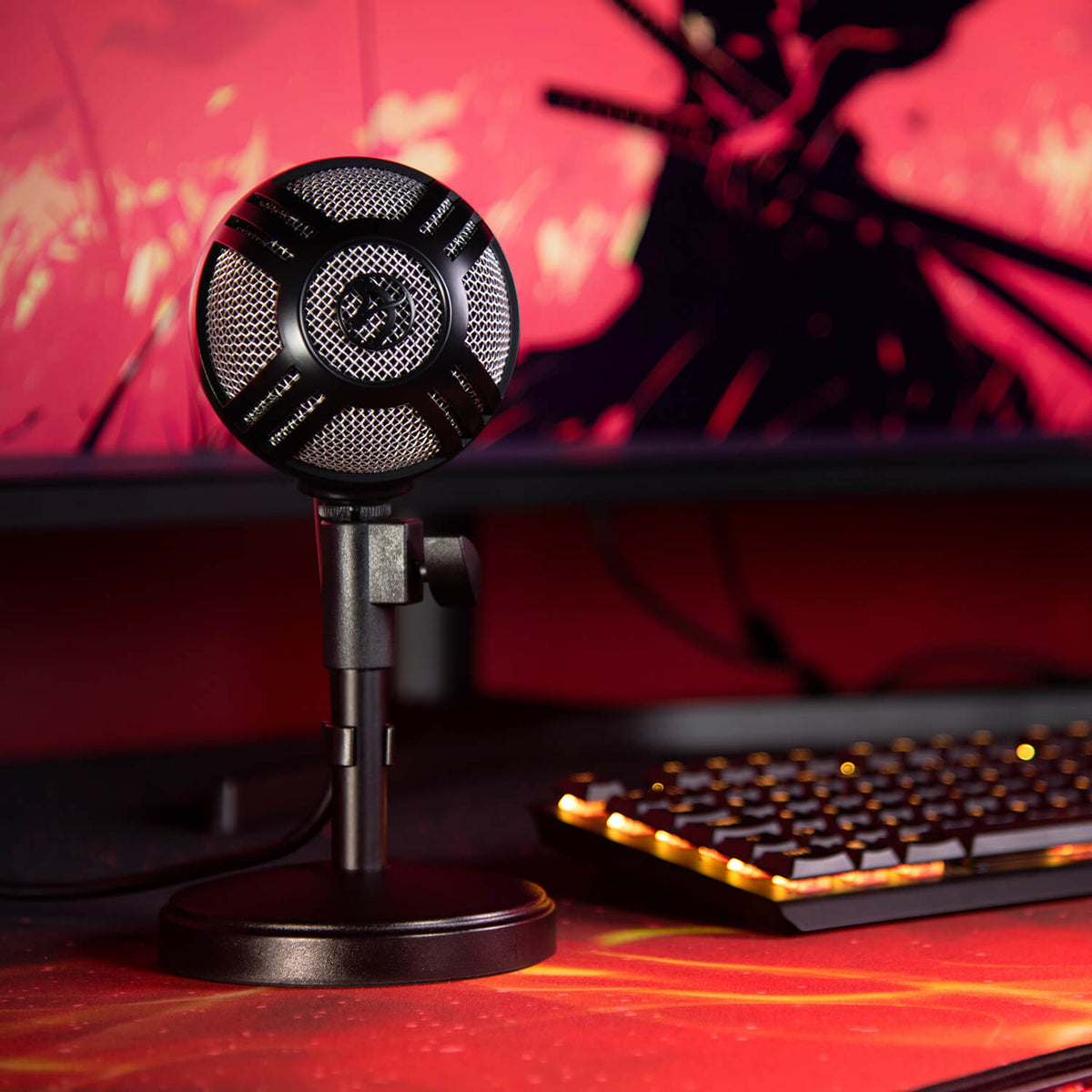 Arozzi Europe’s Sfera Microphone on desk with lit keyboard, monitor, and red background.