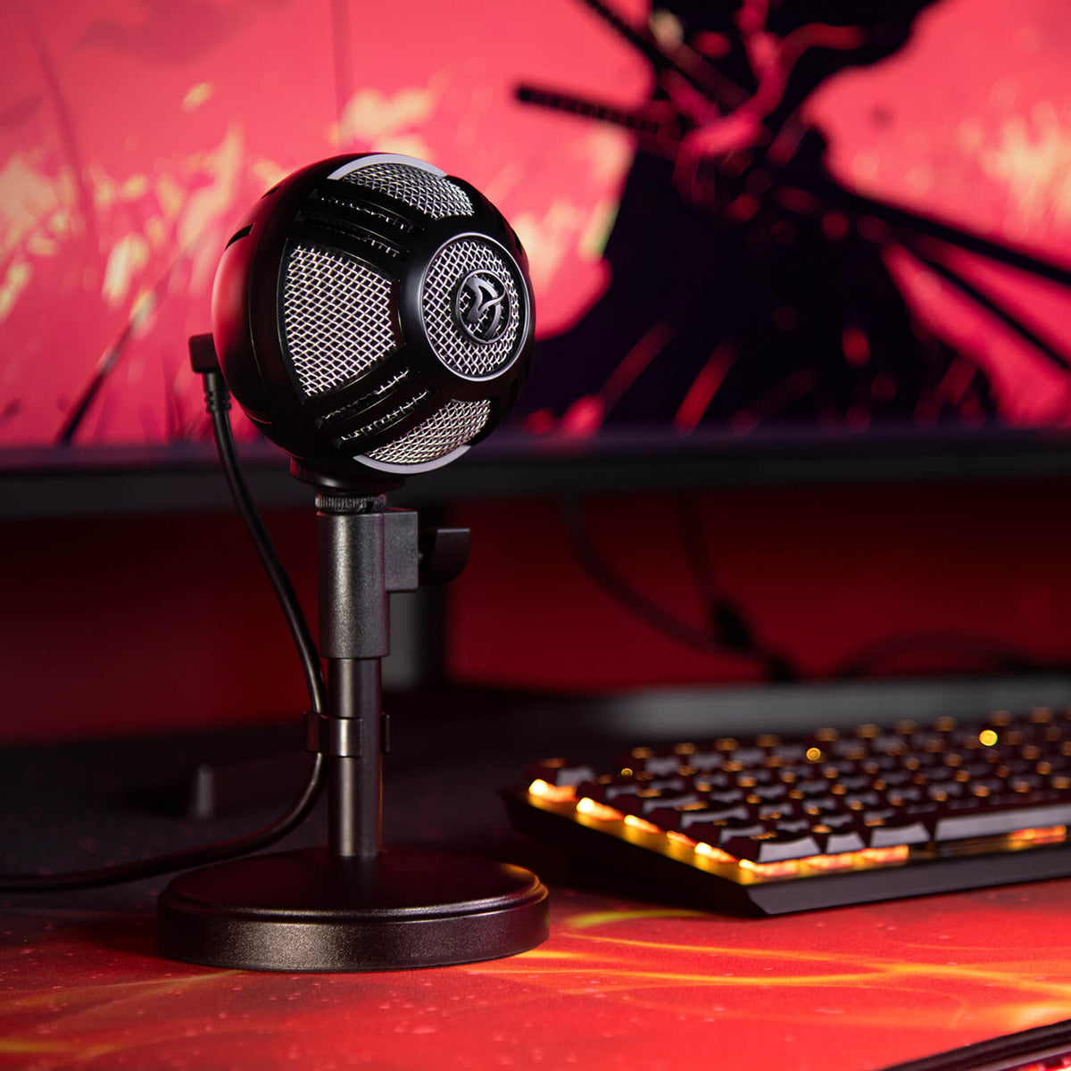 An Arozzi Europe Sfera Pro Microphone sits by a keyboard; a red monitor glows behind it.