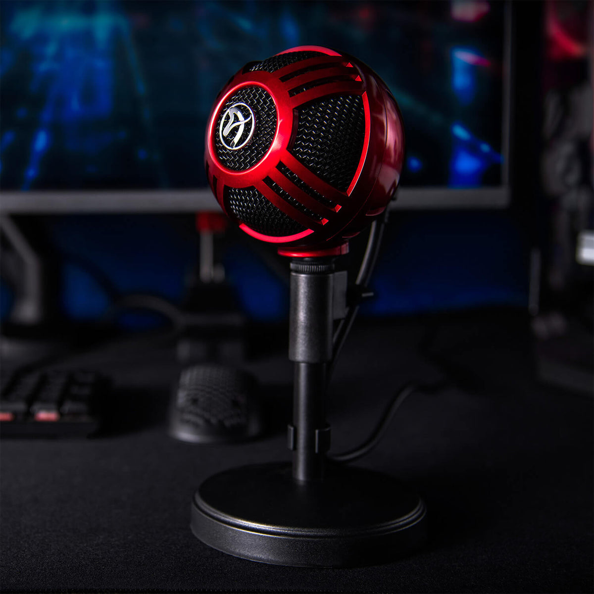 Red and black Arozzi Europe Sfera Microphone on stand in front of monitor and keyboard.
