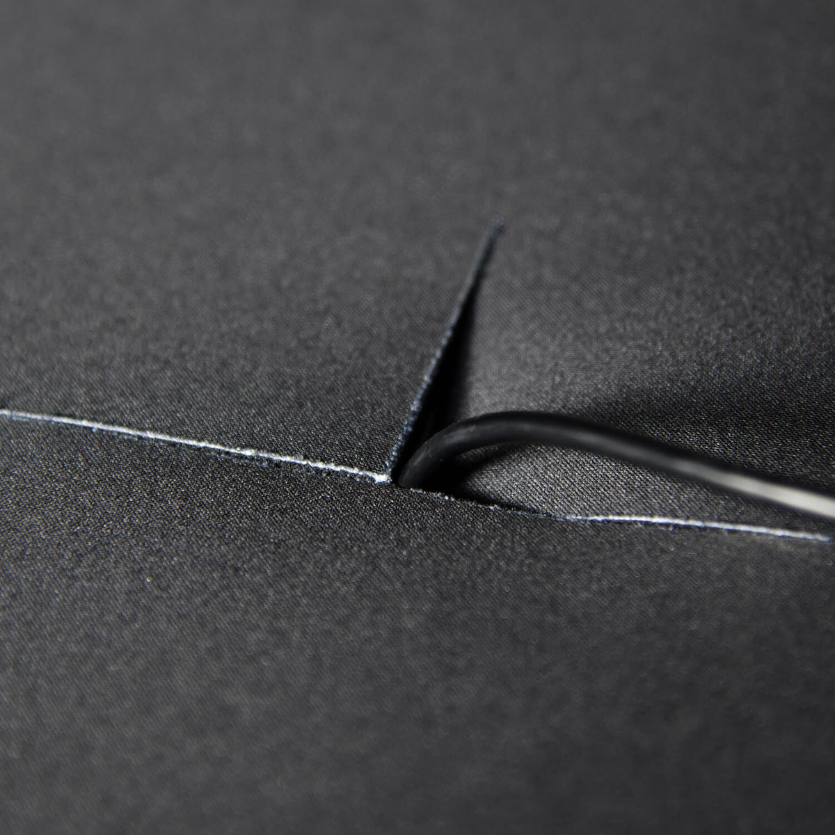 A black cable passes through a slit in a smooth, dark fabric surface.