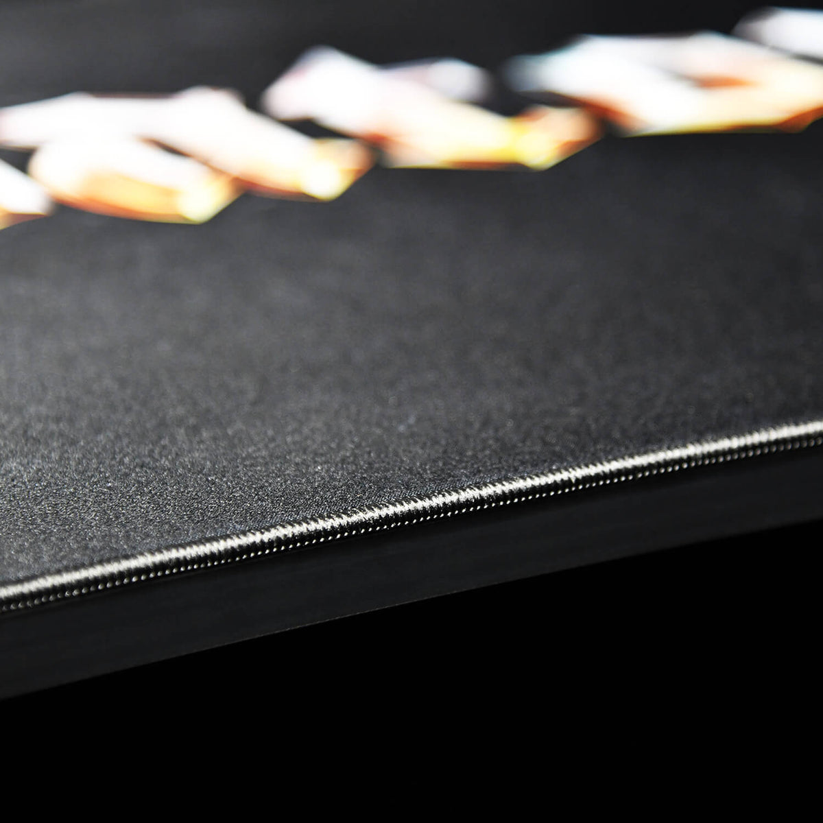 Close-up of a black book cover with visible stitching along the edge and blurred text above.