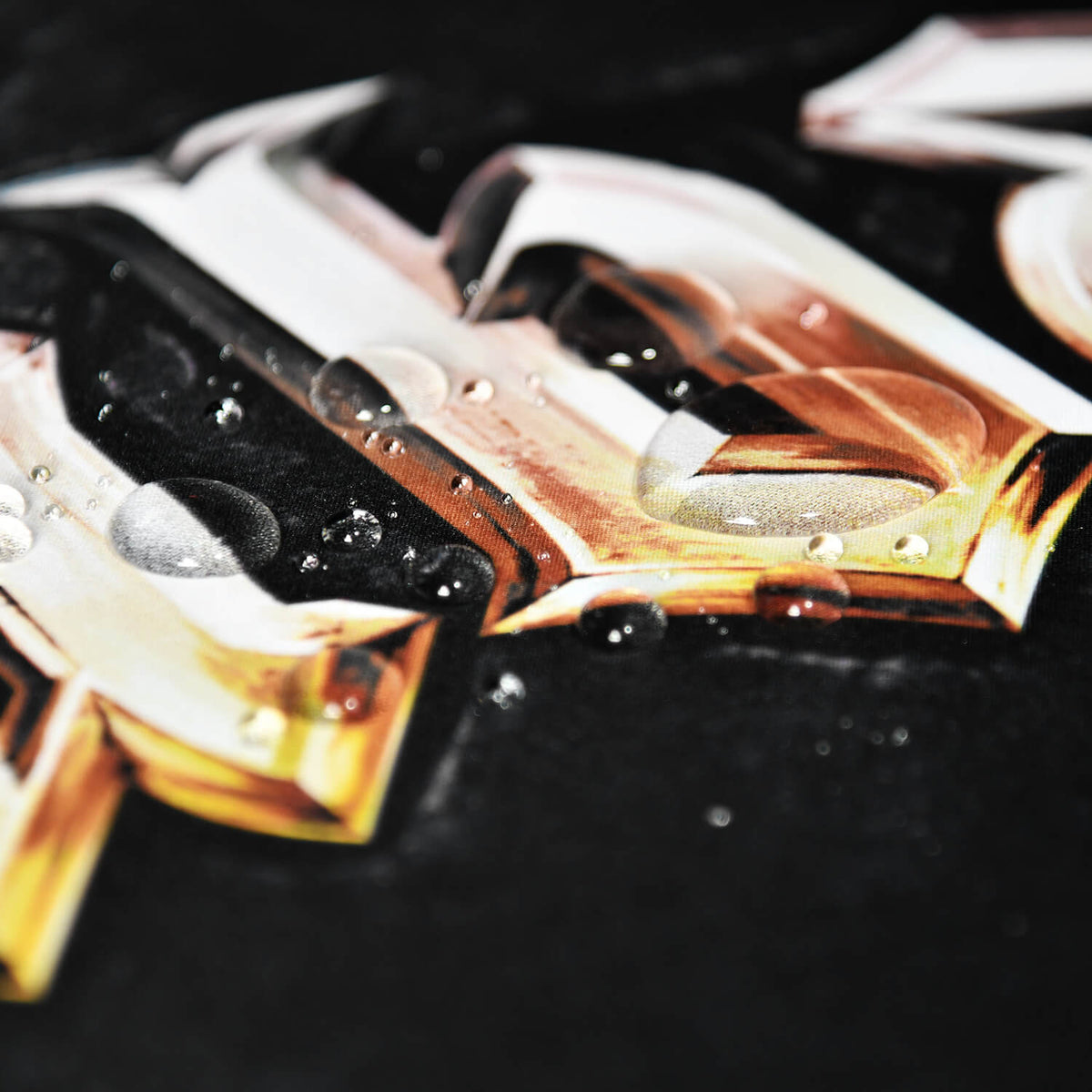 Glossy gold and white letters with water droplets on a black surface.