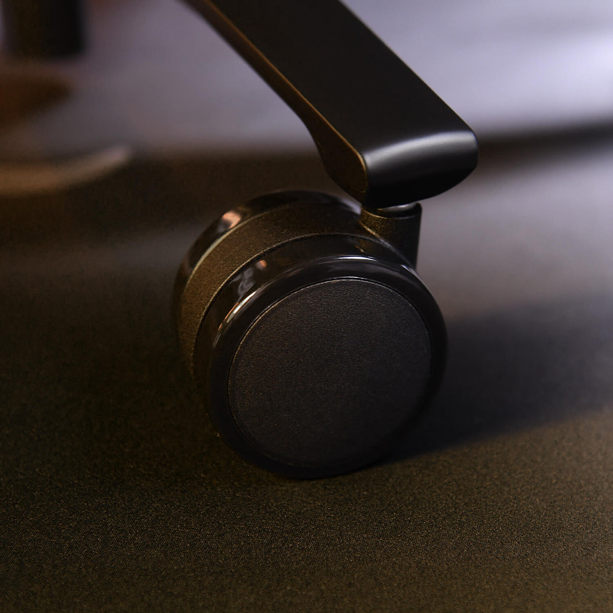 Close-up of a black office chair wheel on a dark floor.