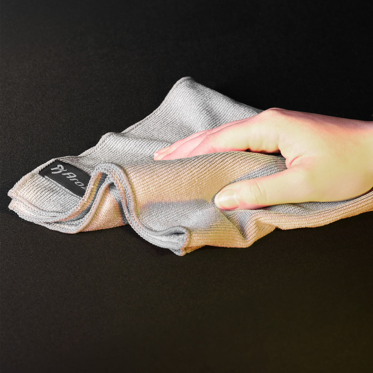 A hand wipes a dark surface with a gray cloth.