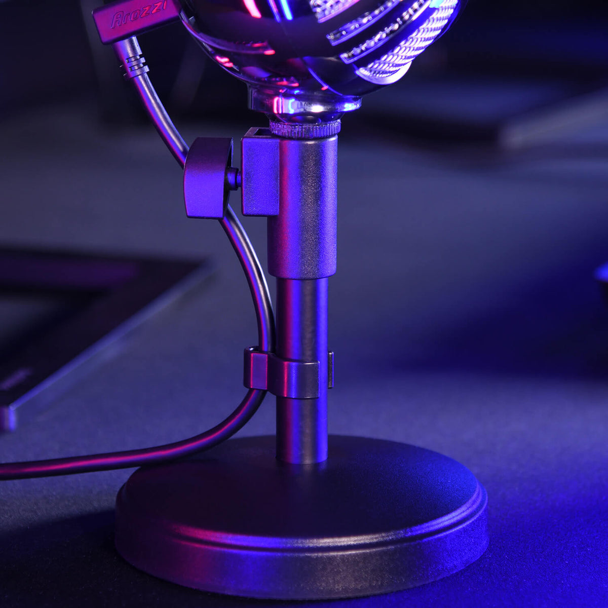 Close-up of a microphone stand with cables, lit by blue and purple lights.