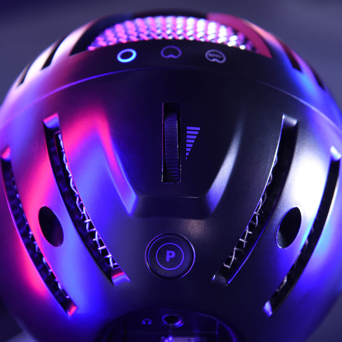 Close-up of a black helmet with glowing blue and pink lights and visible vent details.